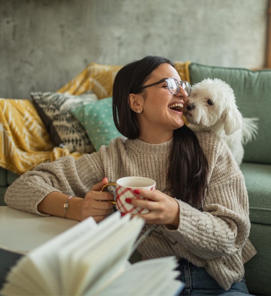 Smiling woman with coffee cup reacts to her little white dog showing her affection. Smiling woman with coffee cup reacts to her little white dog showing her affection.