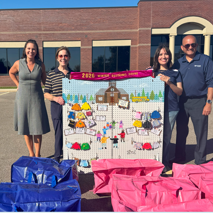 Team members smiling and standing with a results board for the winter clothing drive.